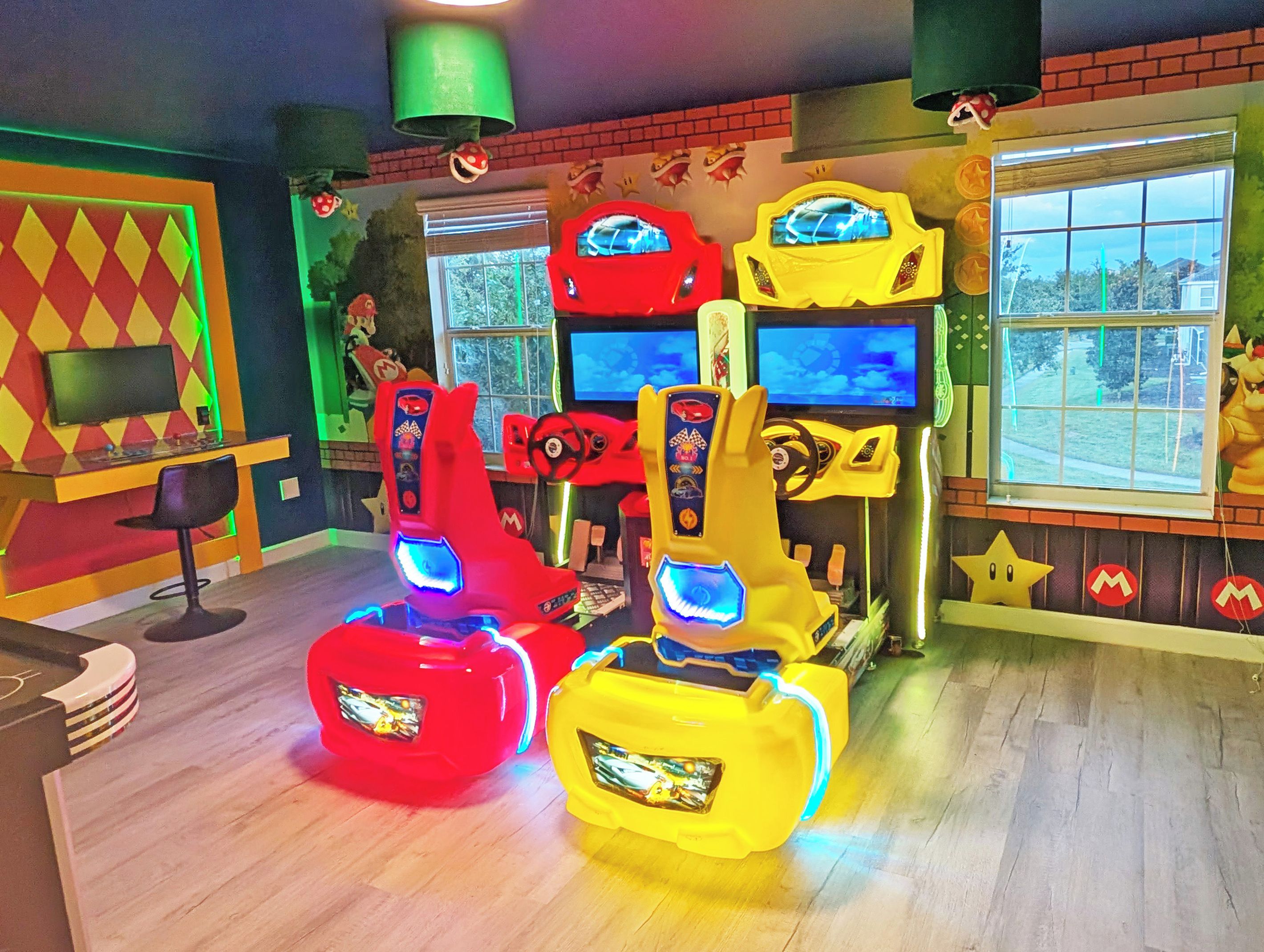 A room with arcade gaming machines, a television, and a window with a view of trees.
