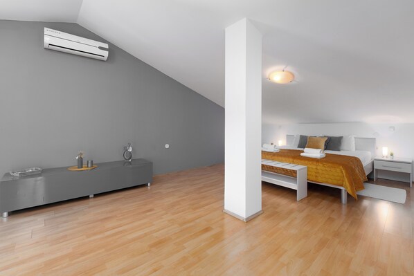 Un dormitorio moderno y minimalista con techo inclinado, una cama con colcha amarilla, una mesita de noche y un banco empotrado.