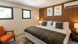 Une chambre d’hôtel avec un grand lit, deux lampes de chevet, une tête de lit en bois et deux fenêtres.