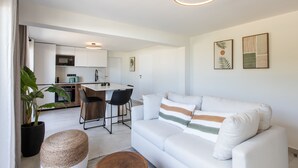 Un salon moderne avec un canapé blanc, un coin repas avec une table et des chaises, une cuisine avec des meubles blancs et une grande plante en pot.