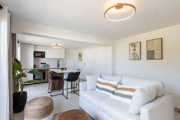 A modern living room with a white sofa, a dining area with a table and chairs, a kitchen with white cabinets, and a large potted plant. - Oceanview - 1bedroom  - Walk to beach (Cole Bay)