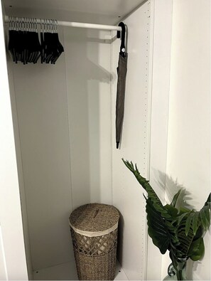 A small, white closet with a hanging rod for clothes, a wicker basket, and a potted plant. - Oceanview - 1bedroom  - Walk to beach (Cole Bay)