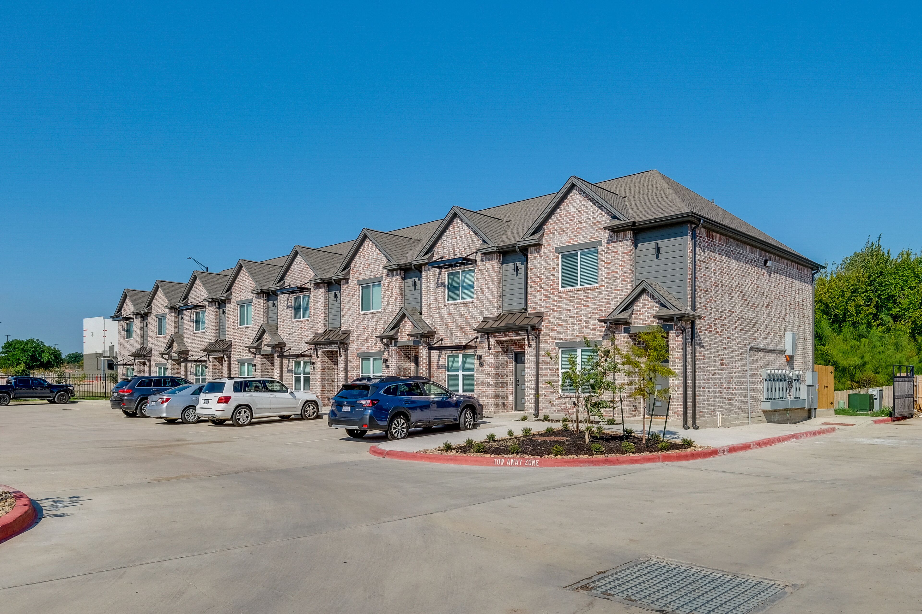 Une rangée de maisons de ville en briques, avec un parking devant.