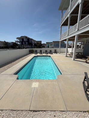 A rectangular swimming pool with a clear blue water surface, surrounded by a concrete deck and a white fence.
