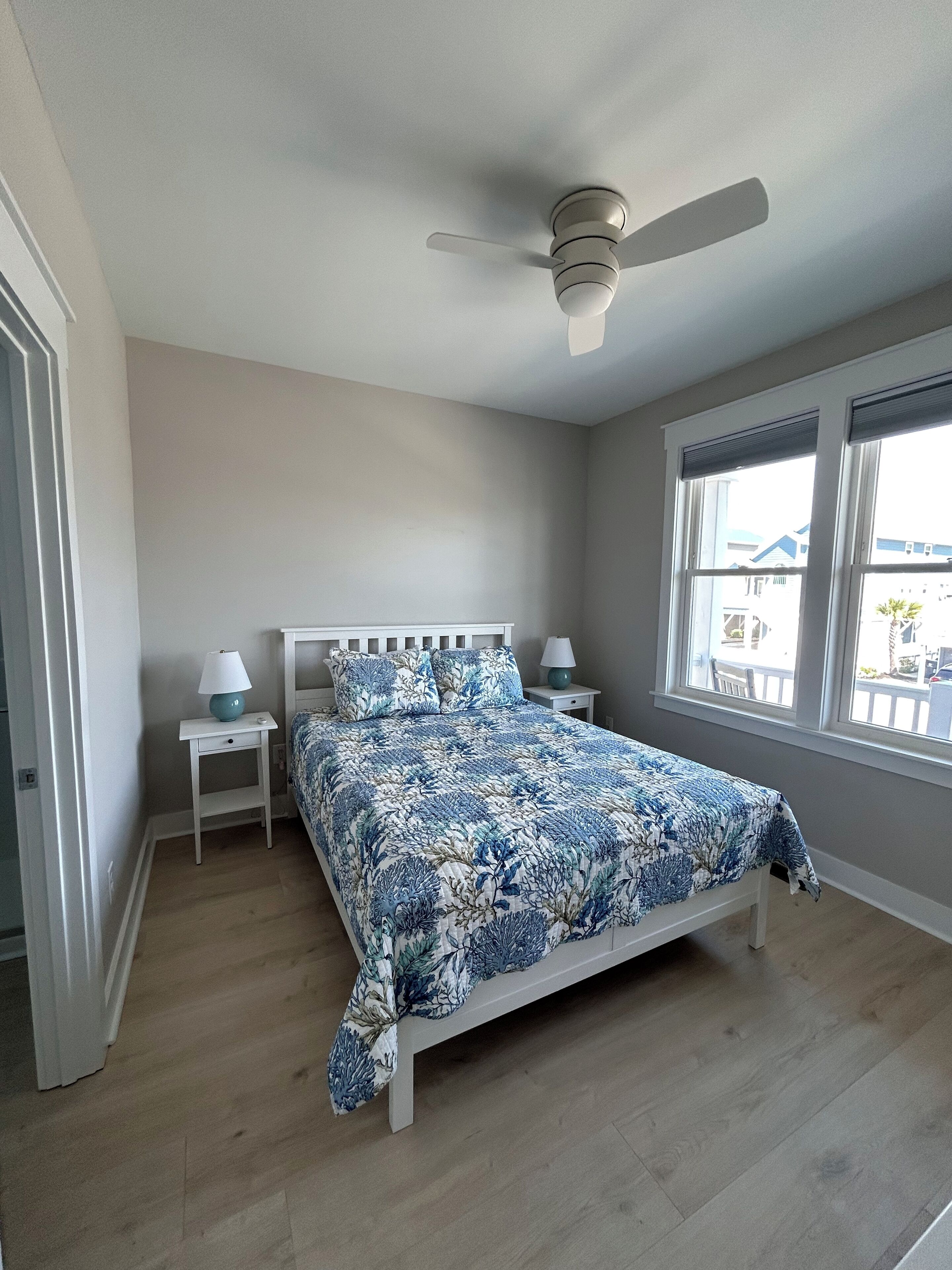 A bedroom with a bed, a ceiling fan, a window, and a nightstand with a lamp.