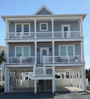 A two-story beachfront house with a balcony on each floor, a covered entryway, and a visible address sign. - Luxury 5 Bedroom, 5.5 Bathroom, Huge Private Pool, Incredible Ocean Views! (Ocean Isle Beach)