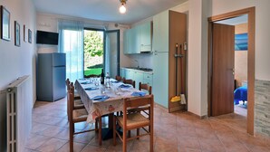 A dining area with a table set for four, a ceiling fan, a kitchen area with cabinets, and a view of the outdoors. - Apartment SMERALDO 3 (manerba del garda solarolo)