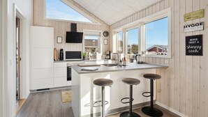 A modern kitchen with wooden paneling, a large island with bar stools, a built-in oven, and a window overlooking the outside. - Lovely home in Sjølund (Sjølund)