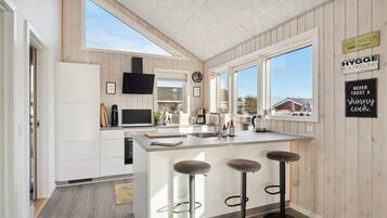 Une cuisine moderne avec un lambris en bois, un grand îlot central doté de tabourets, un four encastré et une fenêtre donnant sur l’extérieur.