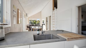 A modern kitchen with a large island, stainless steel sink, and a wooden cutting board. - Lovely home in Sjølund (Sjølund)