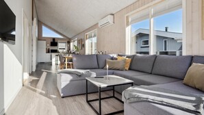 A modern living room with a grey sofa, a coffee table, and a dining area with a wooden table and chairs. - Lovely home in Sjølund (Sjølund)