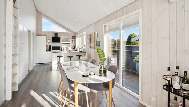 A modern kitchen with white cabinets, a central island, and a dining area with a round table and chairs. - Lovely home in Sjølund (Sjølund)