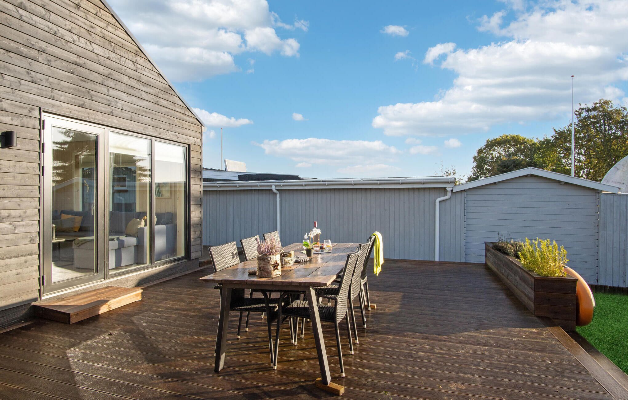 A wooden deck with a table and chairs, a sliding glass door, and a white fence.