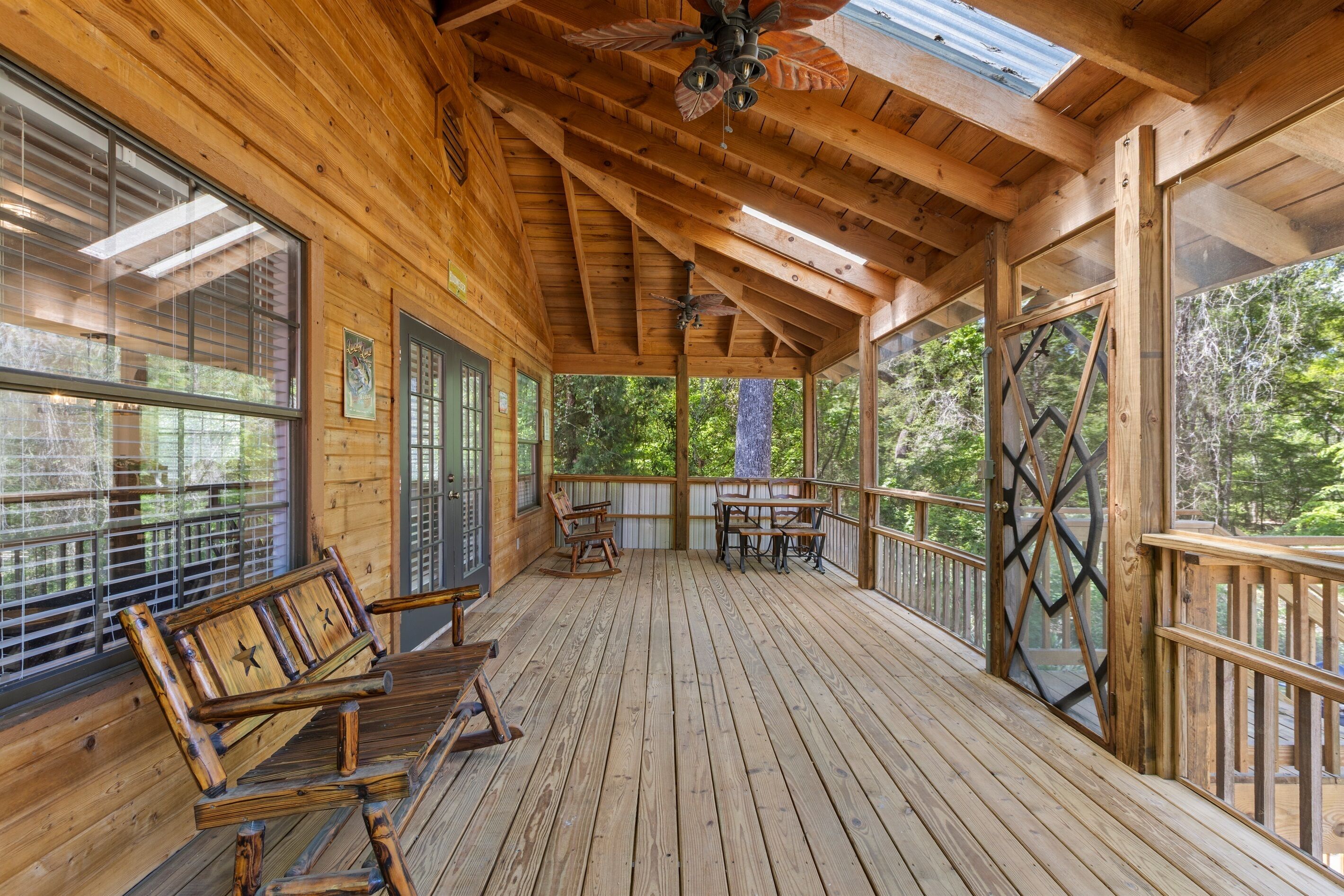 A wooden deck with benches and a table, large windows, and a view of trees.