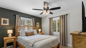A bedroom with a wooden bed, a ceiling fan, two bedside tables with lamps, and a TV on a wooden dresser. - Riverfront Cabin, Private 2 Tier Dock, Ichetucknee (Fort White)