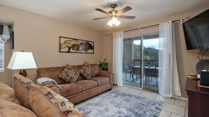 A living room with a brown sofa, a ceiling fan, a TV, and a sliding glass door to a patio.