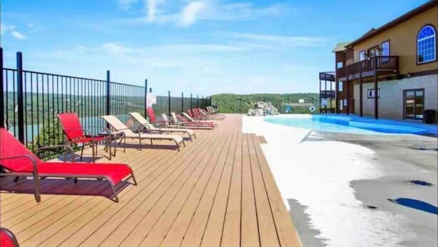 A wooden deck with red lounge chairs, a pool, and a building with a balcony.