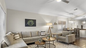 En moderne stue med en hjørnesofa, et rundt sofabord og et spiseområde med bord og stole.