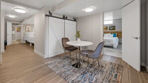 Une chambre d’hôtel moderne, équipée d’un lit, d’une petite table ronde avec deux chaises, d’un grand miroir et offrant une vue sur une autre chambre.