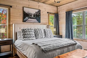 A wooden cabin bedroom with a bed, a nightstand, a window with curtains, and a painting on the wall. - Top 5% · Pet Friendly · Hot Tub · Arcade · Views (Sevierville)