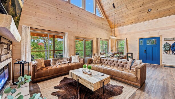 A spacious living room with a large wooden ceiling, leather sofas, a central coffee table, and a stone fireplace. - Top 5% · Pet Friendly · Hot Tub · Arcade · Views (Sevierville)