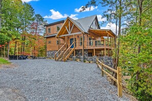 A log cabin with a stone foundation, a wooden deck, and a gravel driveway.