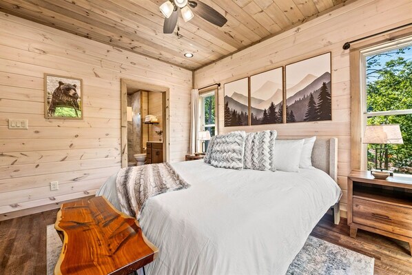 A wooden cabin bedroom with a bed, a wooden coffee table, and a painting of mountains.