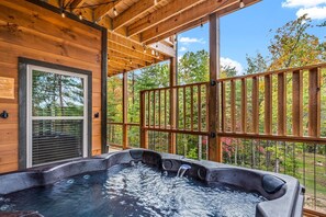 A wooden cabin with a hot tub, large windows, and a view of trees.