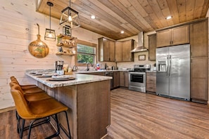 A modern kitchen with wooden cabinetry, a stainless steel refrigerator, and a bar area with stools.