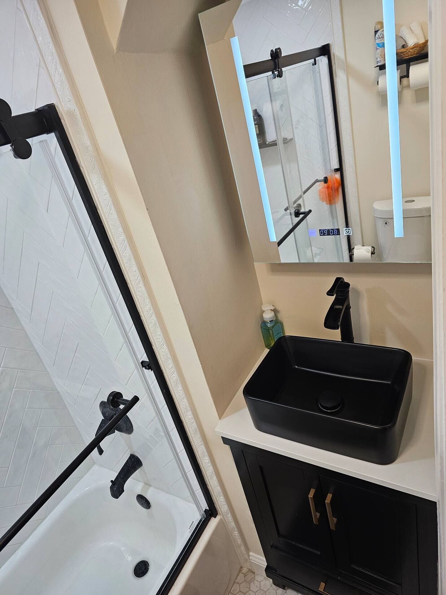 Un baño moderno con cabina de ducha de vidrio, tocador negro con lavabo y espejo sobre el tocador.