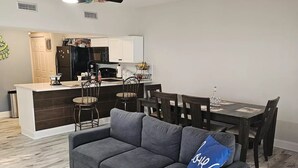 Una sala de estar moderna con un sofá seccional gris, una mesa de comedor con sillas y una cocina al fondo.