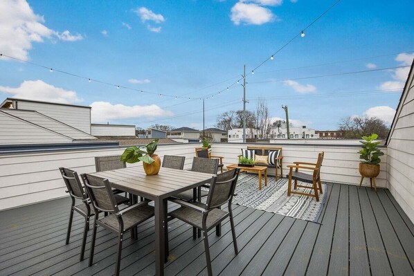 Een dak terras met een houten tafel en stoelen, omgeven door potplanten.