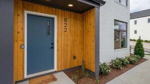 Une maison moderne à deux étages, avec une porte bleue et un revêtement mural en bois, portant le numéro 822, et dotée d’un petit jardin et d’un paillasson.