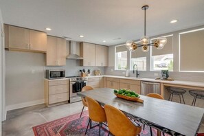Uma cozinha moderna com armários de madeira, fogão de aço inoxidável, micro-ondas e uma área de jantar com mesa e cadeiras.