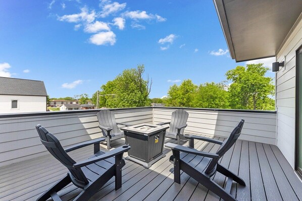 Une terrasse avec quatre chaises Adirondack noires, une table carrée et un barbecue encastré.