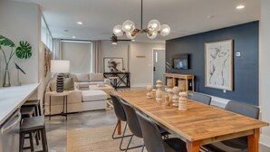 A modern living room with a wooden dining table, black chairs, a sofa, and a chandelier. - Rooftop Fire Pit + Bar ✨ Near Broadway (Nash)