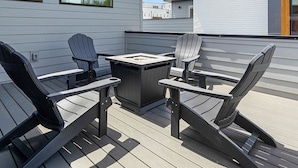 A deck with Adirondack chairs and a fire pit, overlooking a modern building with a white exterior. - Rooftop Fire Pit + Bar ✨ Near Broadway (Nash)