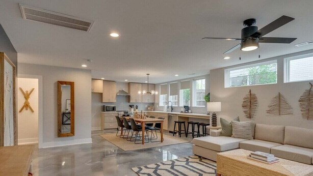 A spacious living area with a kitchen, dining table, and a large window providing natural light. - Rooftop Fire Pit + Bar ✨ Near Broadway (Nash)