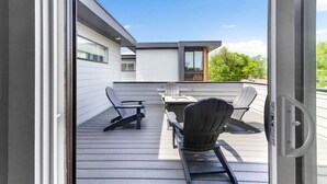 A modern outdoor deck with a table and chairs, a sliding glass door, and a view of a residential building. - Rooftop Fire Pit ~ Bach Parties ~ Sleeps 24! (Nashville)