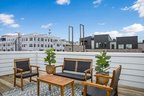 A rooftop terrace with wooden furniture, potted plants, and a view of modern buildings. - 2 Homes - 8 Bedrooms - Sleeps 24! Rooftop Views! (Nashville)