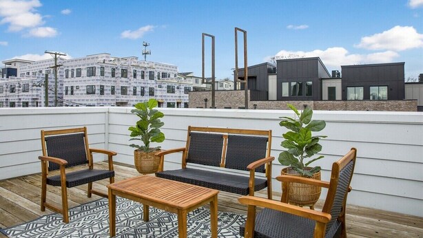 A rooftop terrace with wooden furniture, potted plants, and a view of modern buildings. - Rooftop Lounge ~ Sleeps 12 ~4 bed (Nashville)