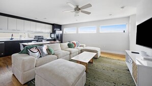 A modern living room with a sofa, ottoman, and coffee table, a kitchen area with cabinets and appliances, and a ceiling fan. - ~ Rooftop lounge ~ 4 bed ~ Sleeps 10! (Nashville)