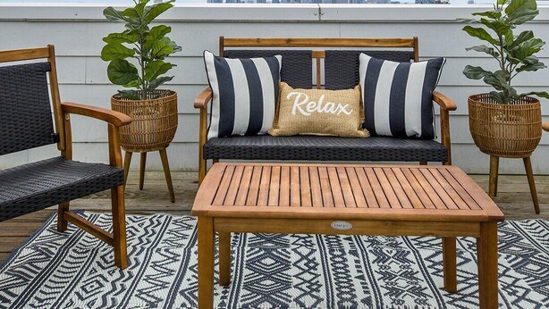 A rooftop patio with a wooden bench, a sofa with striped cushions, and two potted plants.