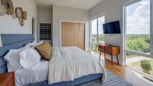 A bedroom with a large bed, a ceiling fan, a TV, and a view of the outdoors.