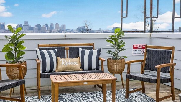 Eine Dachterrasse mit einer Holzliege, zwei Stühlen, einem kleinen Tisch und Topfpflanzen. Ein Schild weist auf einen abgesperrten Bereich hin.