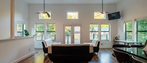 Um quarto espaçoso com um amplo sofá preto, uma mesa de jantar e várias janelas que proporcionam luz natural.