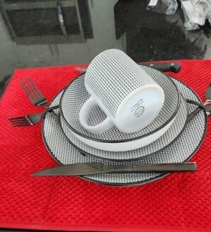 Eine gedeckte Tafel mit einer weißen Tasse, einem schwarz-weißen Untersetzer, einer Gabel, einem Messer und einem Löffel auf einer rot gestreiften Tischdecke.