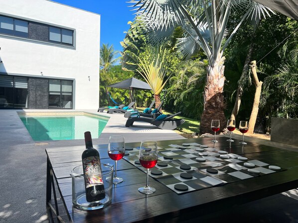 A poolside table with a bottle of wine, glasses, and a chessboard.