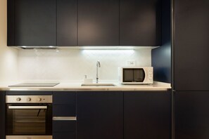 Una cocina moderna con armarios oscuros, horno empotrado, microondas y pileta de acero inoxidable.