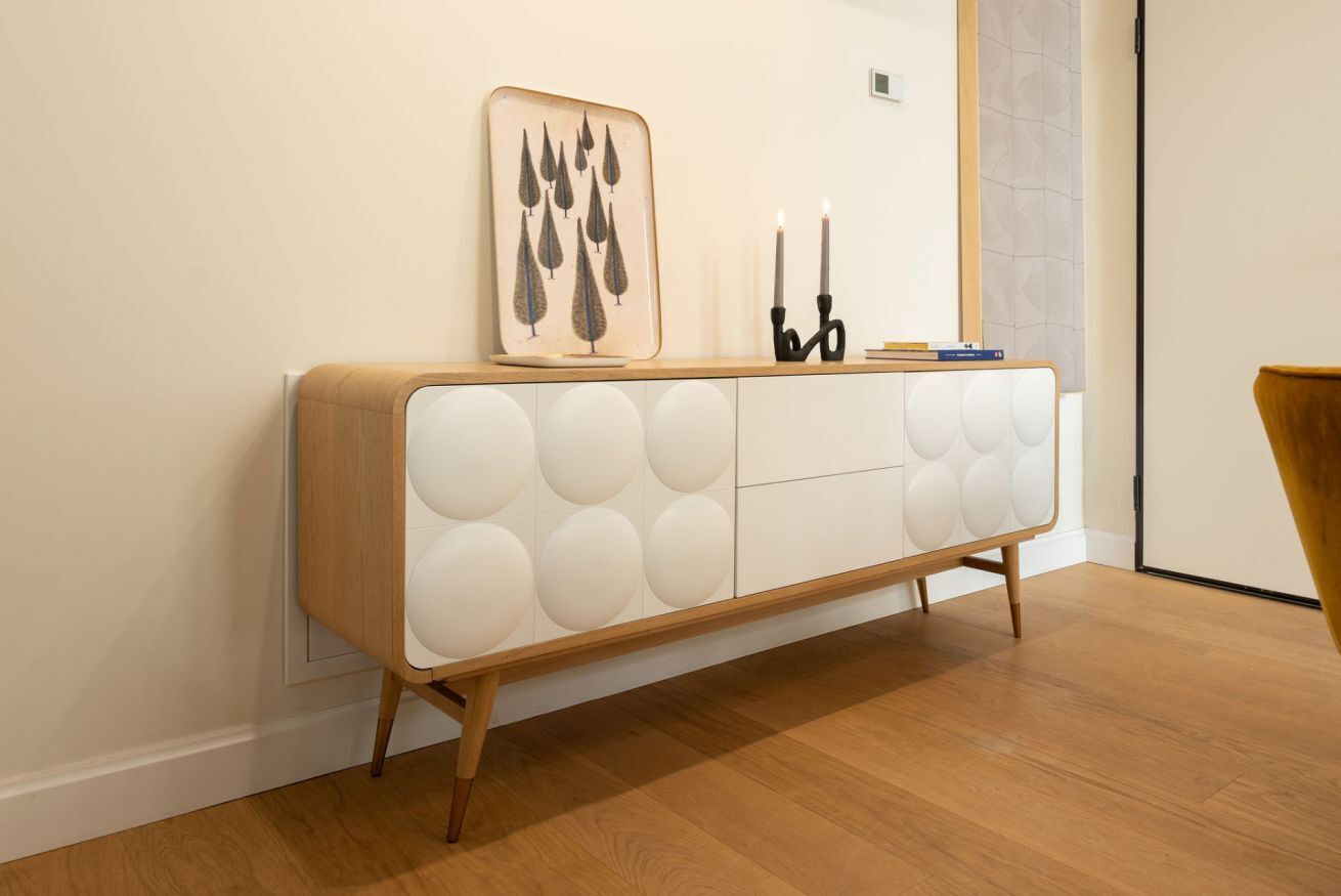 A modern, minimalist console table with a geometric pattern, a framed artwork, and two candles.